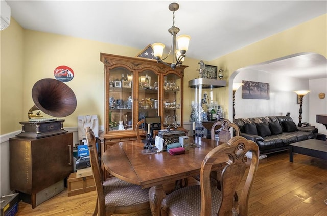 dining room with arched walkways, light wood finished floors, a wall mounted air conditioner, and a notable chandelier