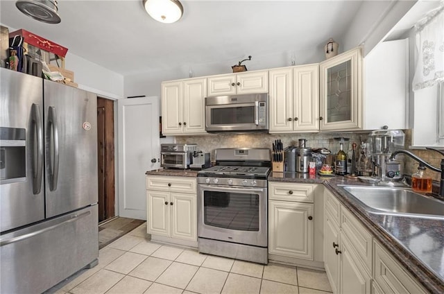 kitchen with stainless steel appliances, tasteful backsplash, glass insert cabinets, light tile patterned flooring, and a sink