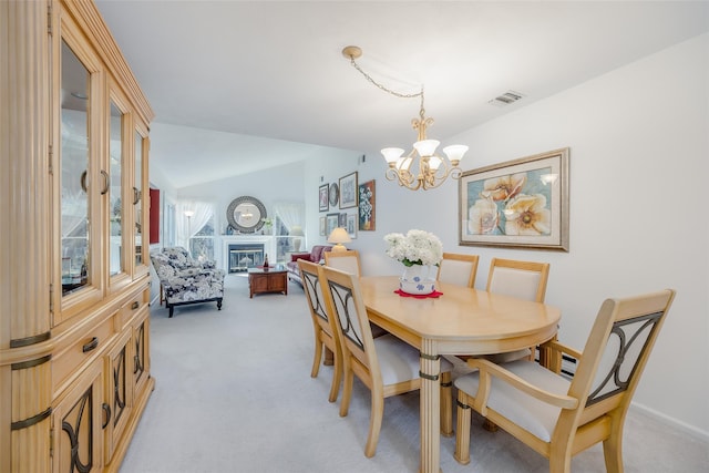 dining space with light colored carpet, visible vents, vaulted ceiling, a glass covered fireplace, and an inviting chandelier