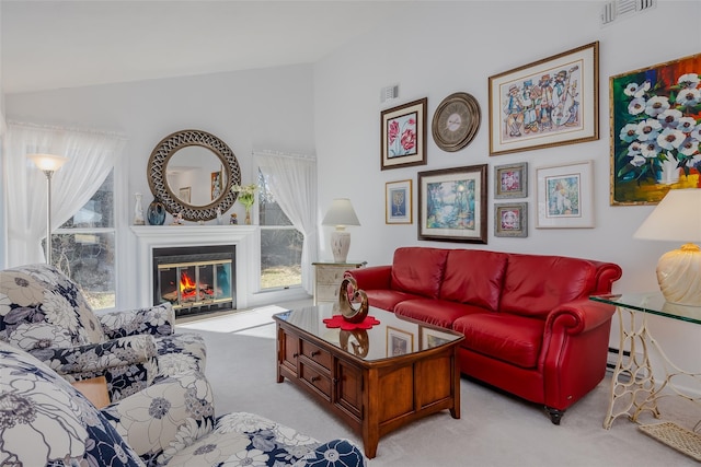 living area featuring lofted ceiling, light carpet, a glass covered fireplace, and visible vents