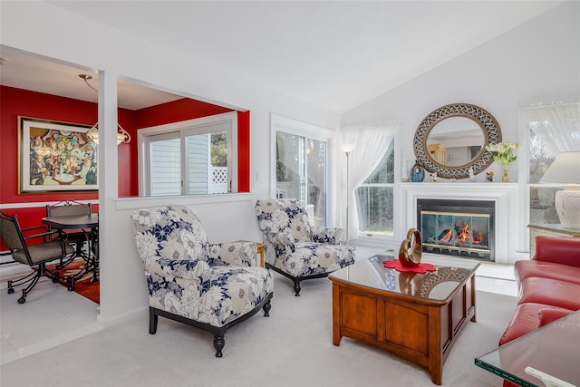 living area featuring plenty of natural light, vaulted ceiling, a glass covered fireplace, and light colored carpet