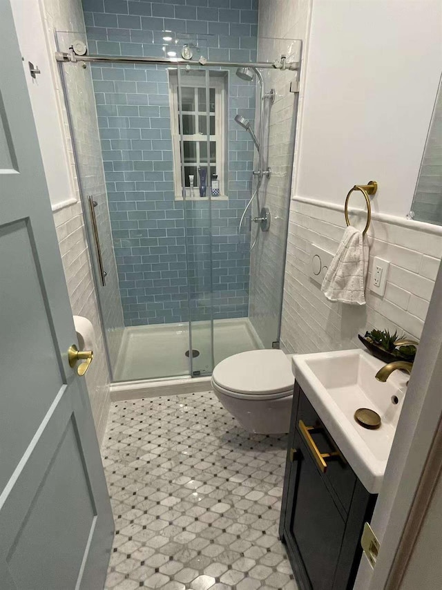 bathroom featuring tile walls, toilet, a stall shower, wainscoting, and vanity