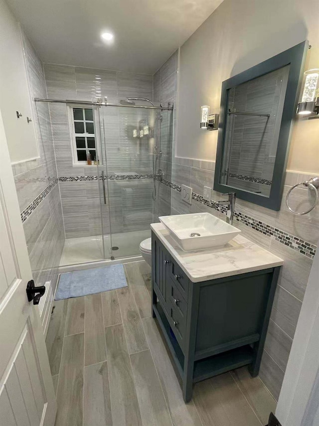 bathroom with toilet, wood tiled floor, vanity, a shower stall, and tile walls