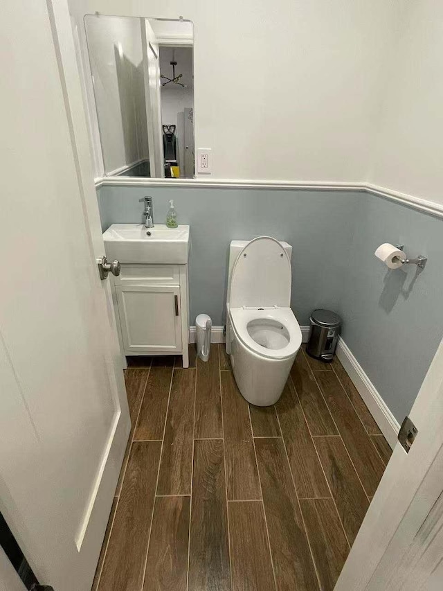 bathroom with toilet, vanity, baseboards, and wood finish floors