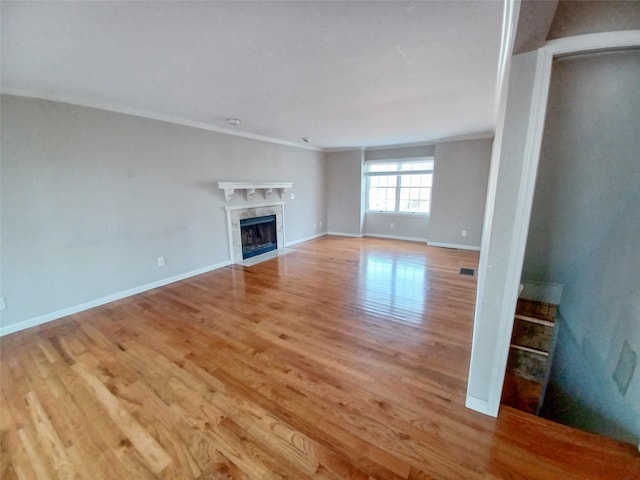 unfurnished living room featuring light wood-style flooring, a premium fireplace, visible vents, baseboards, and crown molding