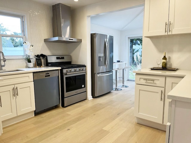 kitchen with wall chimney range hood, appliances with stainless steel finishes, light countertops, and a sink