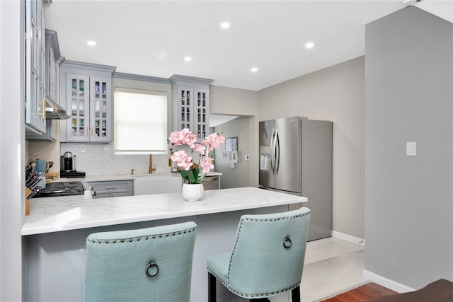 kitchen with gray cabinetry, a peninsula, a breakfast bar, stainless steel fridge with ice dispenser, and glass insert cabinets