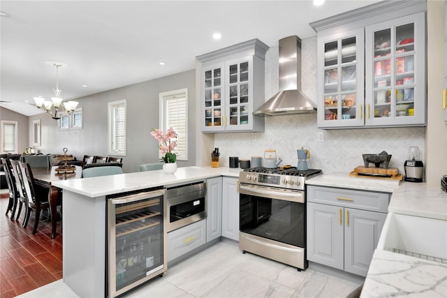 kitchen featuring beverage cooler, appliances with stainless steel finishes, gray cabinets, wall chimney exhaust hood, and glass insert cabinets