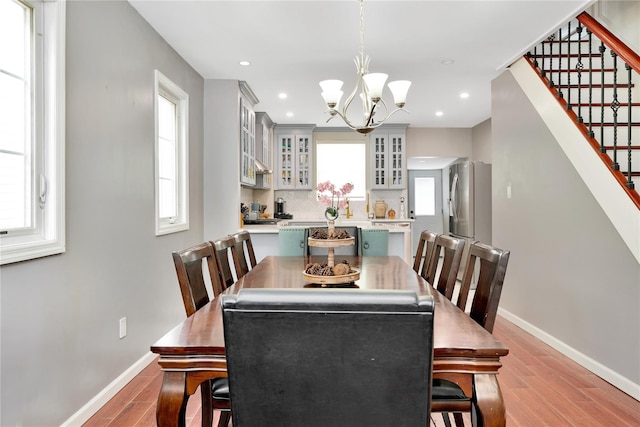 dining space with light wood-style floors, an inviting chandelier, baseboards, and stairs