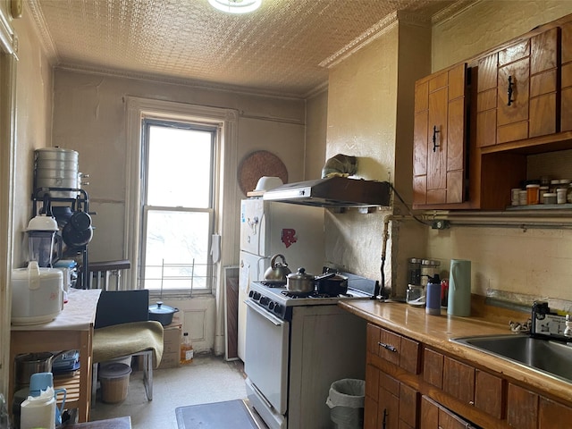 kitchen featuring ornamental molding, brown cabinetry, a sink, and white range with gas cooktop