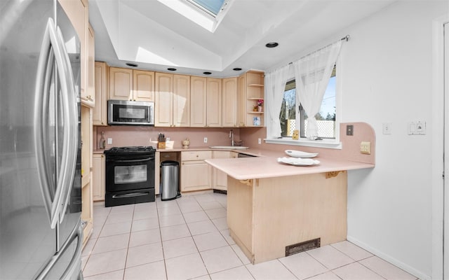 kitchen with a peninsula, a sink, appliances with stainless steel finishes, light brown cabinetry, and lofted ceiling with skylight