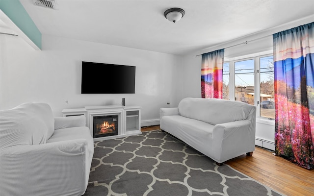 living room with a glass covered fireplace, visible vents, baseboard heating, and wood finished floors