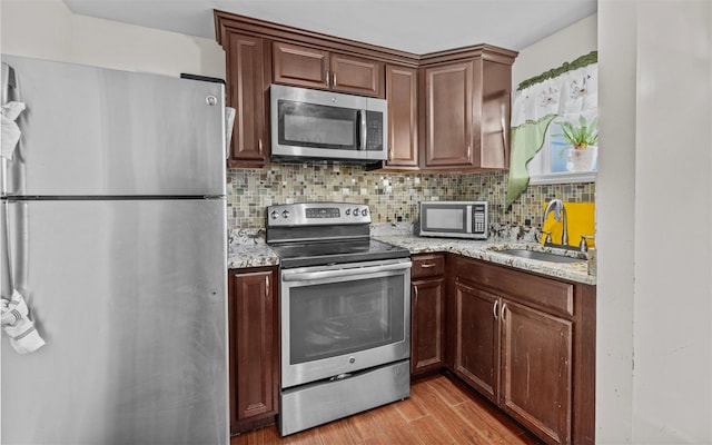 kitchen featuring backsplash, light wood-style flooring, appliances with stainless steel finishes, a sink, and light stone countertops