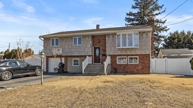 split foyer home with aphalt driveway, brick siding, a chimney, an attached garage, and fence