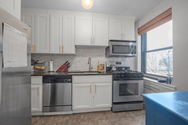 kitchen with dark countertops, white cabinetry, stainless steel appliances, and a sink