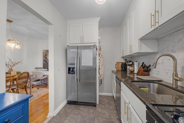 kitchen with tasteful backsplash, dark stone countertops, stainless steel appliances, white cabinetry, and a sink