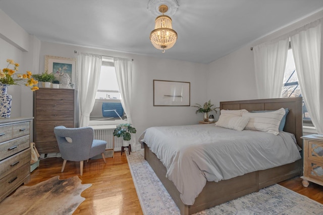 bedroom with radiator, light wood-style floors, and a chandelier