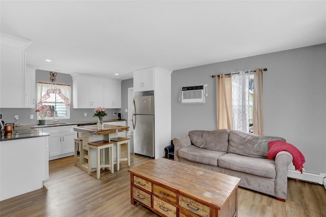 living area featuring a baseboard radiator, a wall unit AC, light wood finished floors, and recessed lighting