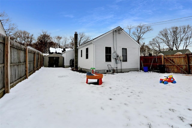 snow covered house with a shed, a chimney, an outdoor structure, and a fenced backyard