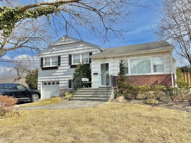 split level home with driveway, brick siding, an attached garage, and a front yard