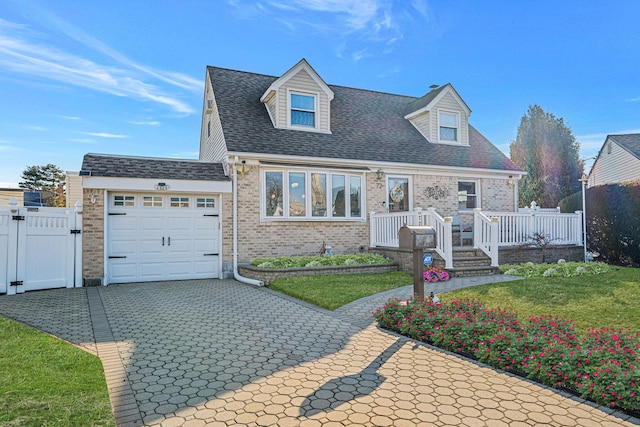 new england style home with a garage, brick siding, a shingled roof, decorative driveway, and a front yard