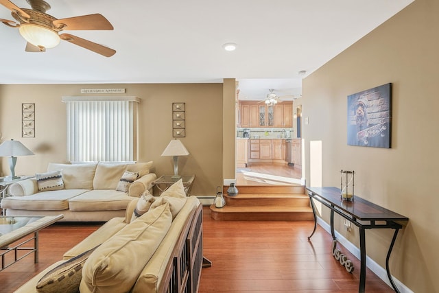 living room with baseboard heating, wood finished floors, a ceiling fan, and baseboards