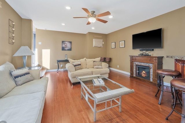 living room featuring a glass covered fireplace, recessed lighting, baseboards, and wood finished floors