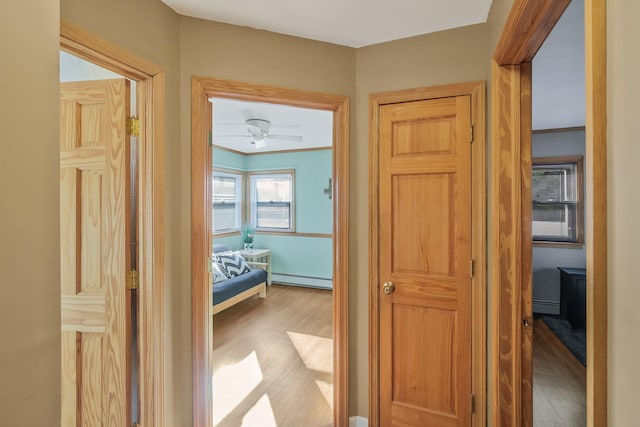 corridor featuring ornamental molding, baseboard heating, and wood finished floors