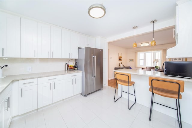 kitchen with pendant lighting, a breakfast bar area, white cabinets, high quality fridge, and black microwave