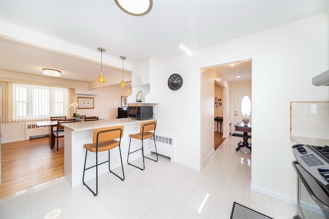 kitchen with radiator, a breakfast bar area, a peninsula, light countertops, and white cabinetry