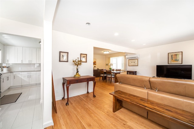 living room featuring baseboards, an AC wall unit, and light wood-style floors