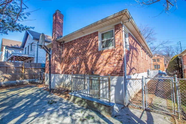 view of side of property with a gate, brick siding, fence, and a chimney