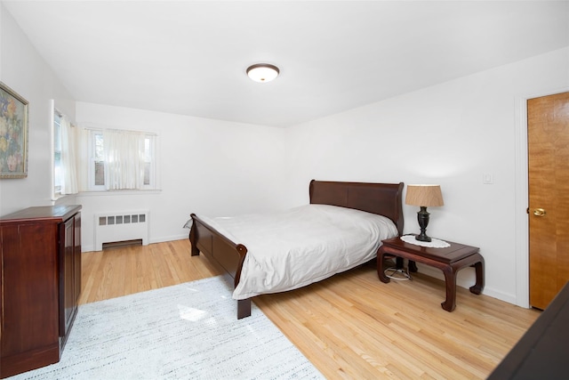 bedroom with radiator heating unit, light wood-type flooring, and baseboards