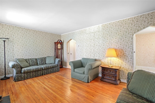 living area featuring arched walkways, wood finished floors, baseboards, and wallpapered walls