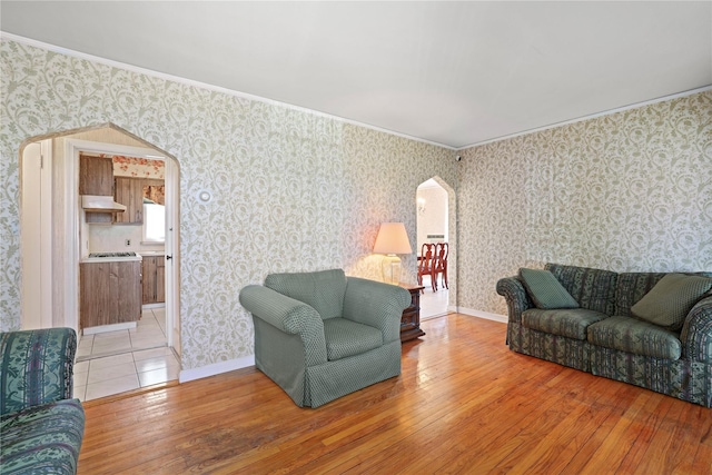 living room with arched walkways, light wood-type flooring, baseboards, and wallpapered walls