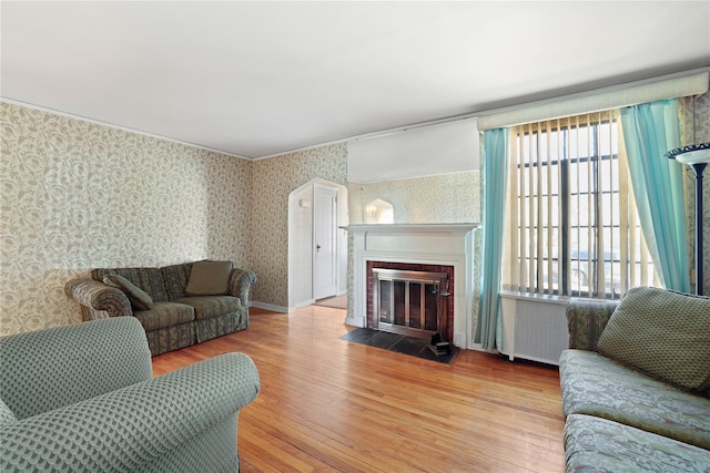 living room featuring radiator, a brick fireplace, wood finished floors, and wallpapered walls