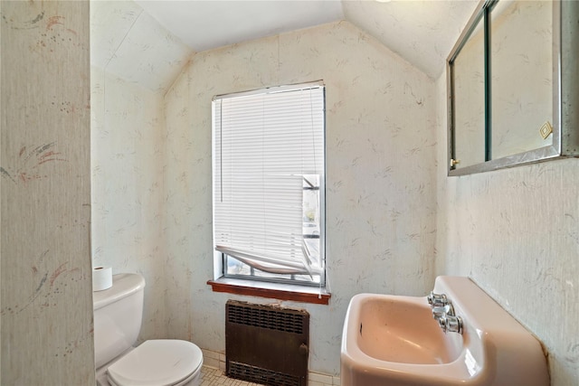 half bath with toilet, a sink, vaulted ceiling, and radiator heating unit