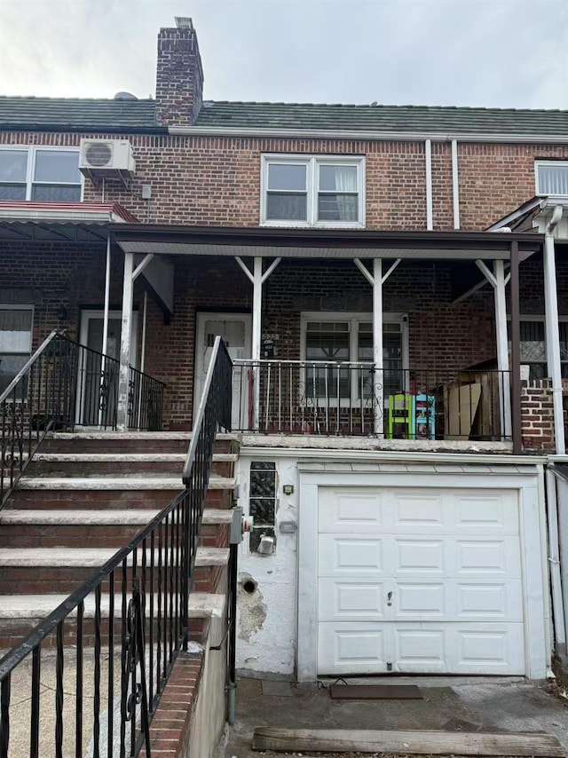 multi unit property with brick siding, a chimney, covered porch, a garage, and stairs