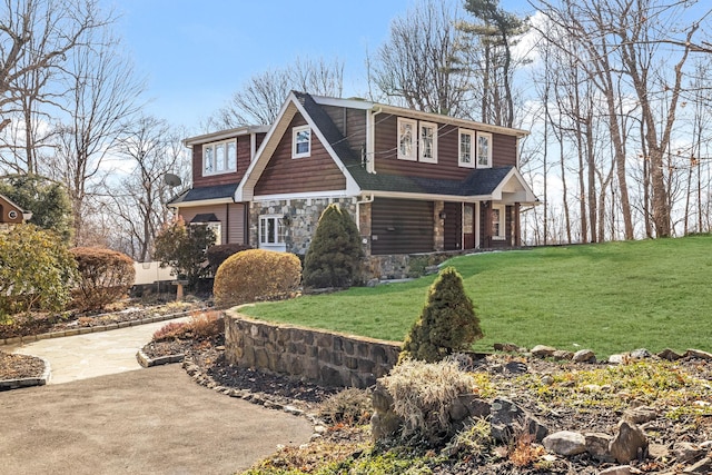 view of front of home with stone siding, roof with shingles, and a front lawn