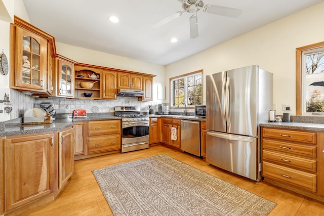 kitchen featuring stainless steel appliances, backsplash, glass insert cabinets, and under cabinet range hood