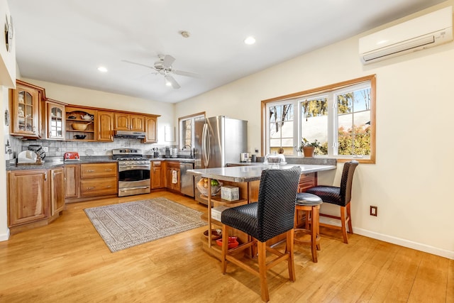 kitchen featuring appliances with stainless steel finishes, brown cabinets, a wall mounted air conditioner, under cabinet range hood, and backsplash