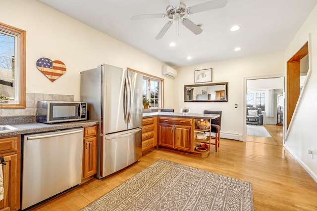 kitchen with stainless steel appliances, light wood-style flooring, brown cabinetry, a wall mounted air conditioner, and a peninsula