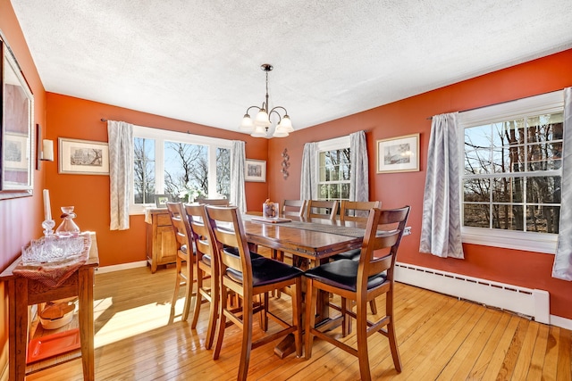 dining area featuring light wood finished floors, baseboards, a baseboard radiator, a textured ceiling, and a notable chandelier