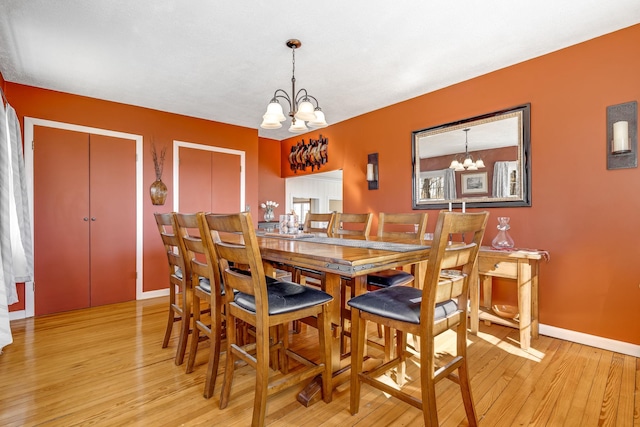 dining space with light wood-type flooring, baseboards, and an inviting chandelier