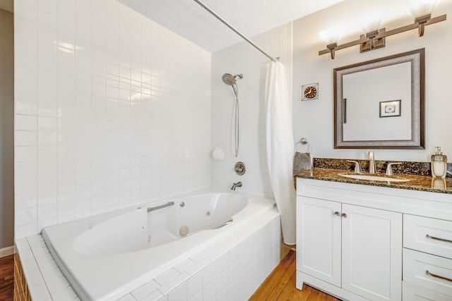 full bath with a combined bath / shower with jetted tub, vanity, a textured ceiling, and wood finished floors