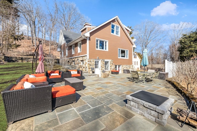 rear view of house with stone siding, a patio area, fence, and an outdoor living space