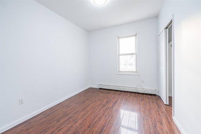 unfurnished bedroom with dark wood-style floors, baseboard heating, a closet, and baseboards