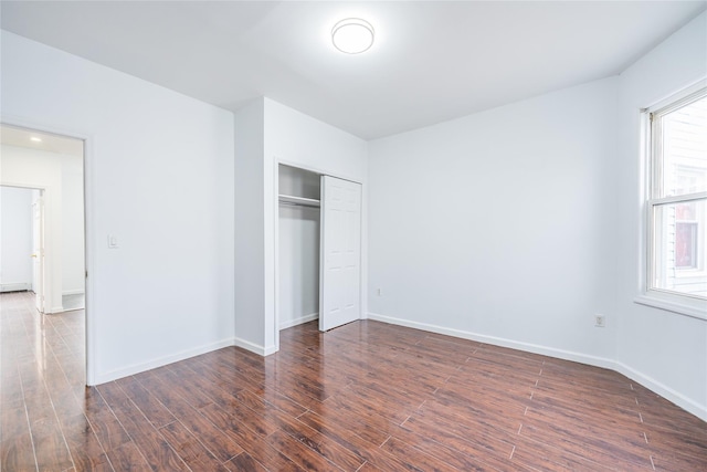 unfurnished bedroom featuring a closet, baseboards, and dark wood-type flooring