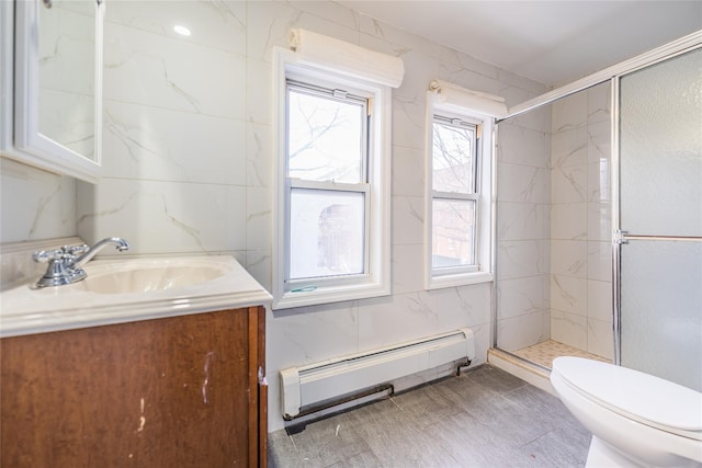 bathroom with a stall shower, toilet, baseboard heating, vanity, and tile walls