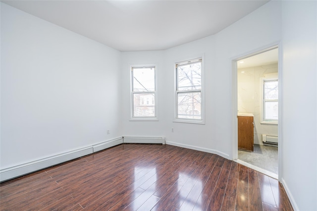 spare room featuring dark wood-type flooring, a baseboard heating unit, and baseboards